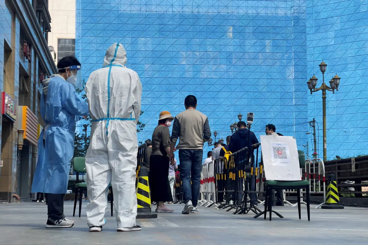Workers in protective suits stand next to people lining up a makeshift nucleic acid testing site during a mass testing in Chaoyang district of Beijing on May 4, 2022. (Alessandro Diviggiano/Reuters)