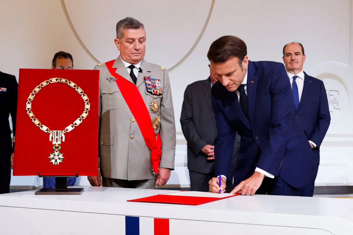 France's Military Chief of Staff to the presidency Benoit Puga stands next to French President Emmanuel Macron (R) signing a document as he is sworn-in for a second term as president after his reelection, during a ceremony at the Elysee Palace in Paris on May 7, 2022. (Gonzalo Fuentes/Pool via Reuters)