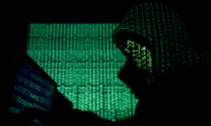 A hooded man holds a laptop computer as cyber code is projected on him in this illustration picture taken on May 13, 2017. (Kacper Pempel/Illustration/Reuters, File Photo0