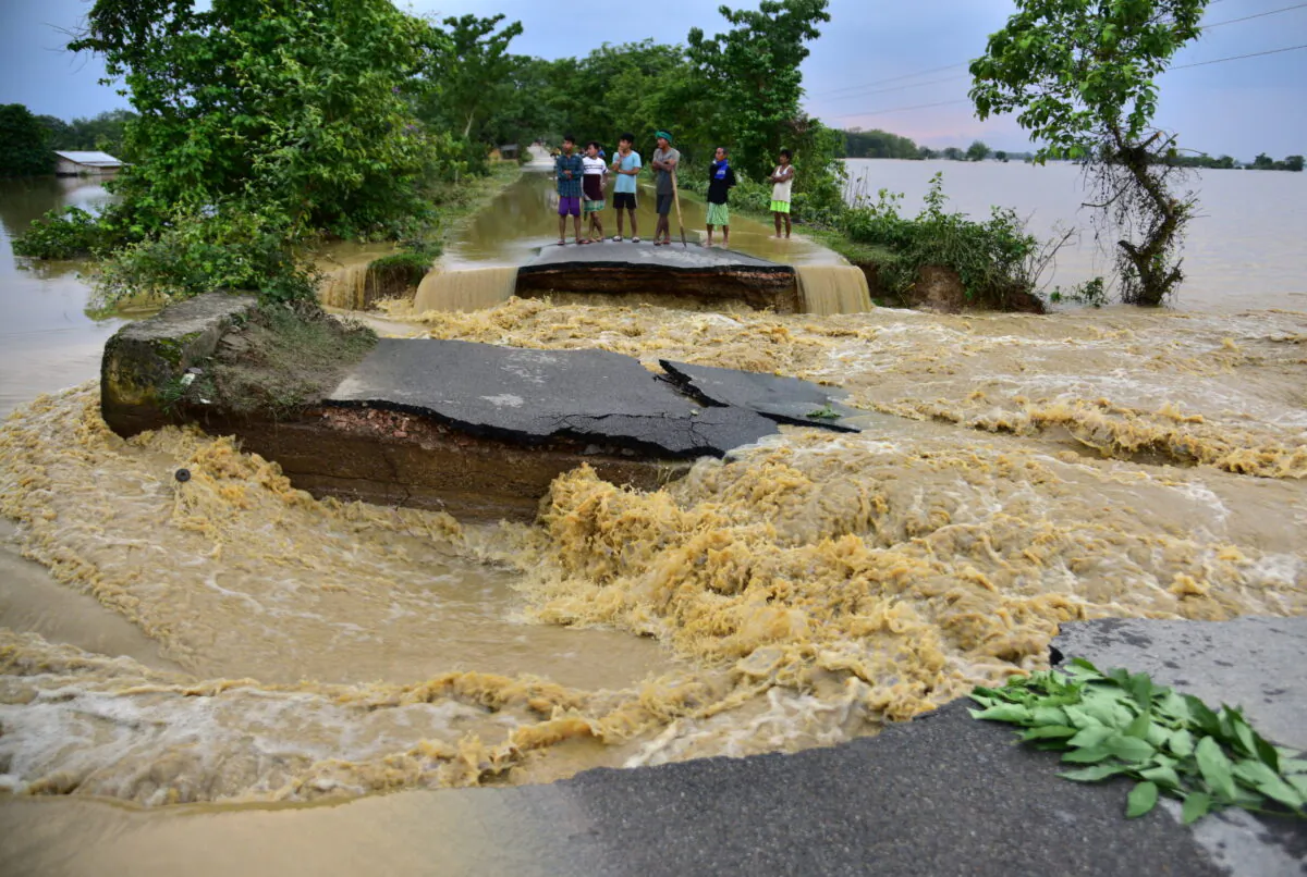 People stand on a road damaged by the flood waters after heavy rains in Nagaon district, in the northeastern state of Assam, India, on May 19, 2022. (Anuwar Hazarika/Reuters)