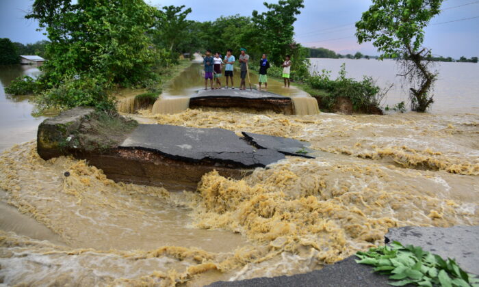 People stand on a road damaged by the flood waters after heavy rains in Nagaon district, in the northeastern state of Assam, India, on May 19, 2022. (Anuwar Hazarika/Reuters)