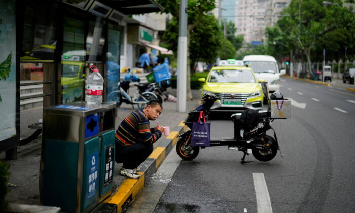A delivery worker, who says he is living at a bus stop because he has been unable to return home for weeks due to the lockdown, brushes his teeth on a street in Shanghai on May 12, 2022. (Aly Song/Reuters)