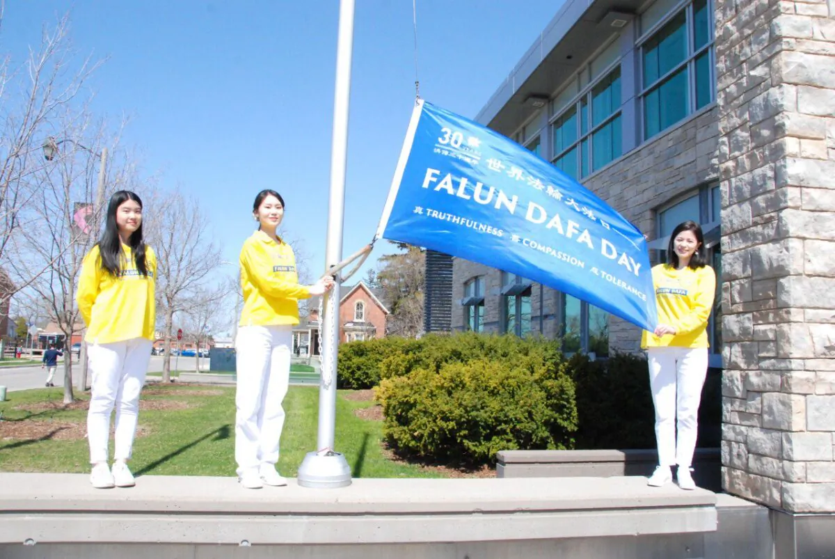 Falun Dafa adherents raise a flag in celebration of the 30th anniversary of the spread of the spiritual practice, in the City of Milton, Ont. on April 29, 2022. (Arek Rusek/The Epoch Times)