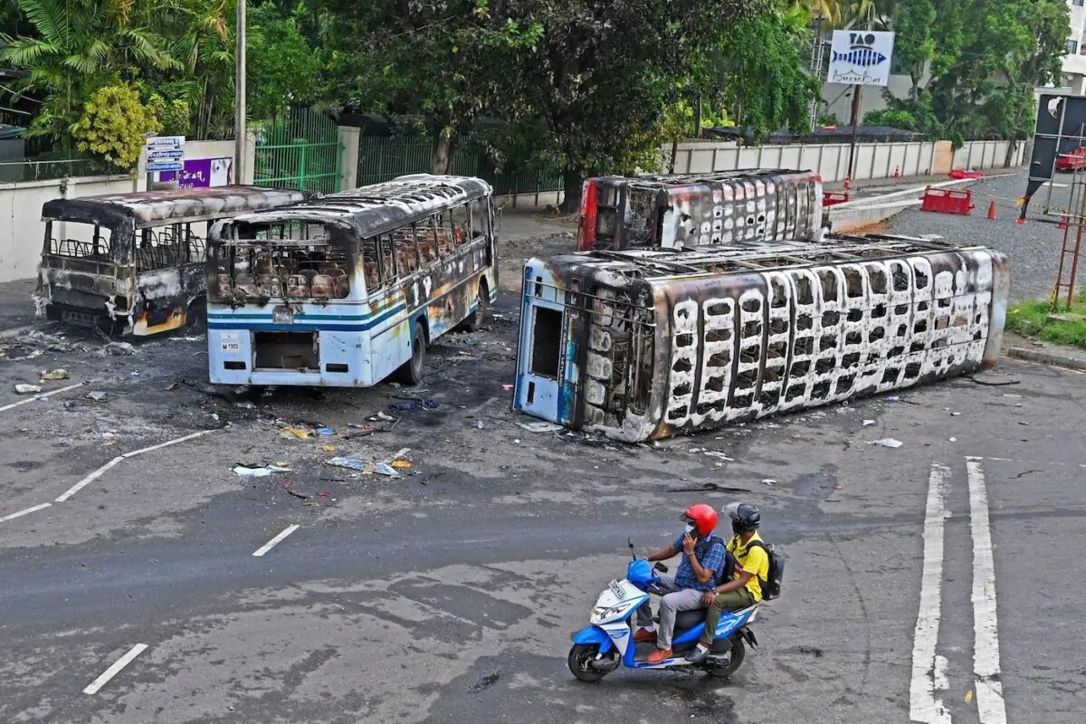 Men on a scooter ride past the burnt buses near Sri Lanka's former prime minister Mahinda Rajapaksa's official residence 'Temple Trees', a day after they were torched by protesters in Colombo on May 10, 2022. (Ishara S. Kodikara/AFP via Getty Images)