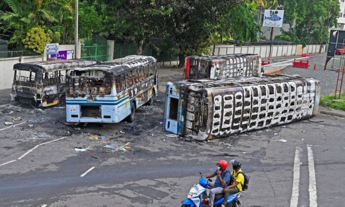 Men on a scooter ride past the burnt buses near Sri Lanka's former prime minister Mahinda Rajapaksa's official residence 'Temple Trees', a day after they were torched by protesters in Colombo on May 10, 2022. (Ishara S. Kodikara/AFP via Getty Images)