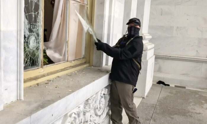 A suspicious actor vandalizes a Capitol window on Jan. 6, 2021. The man was caught on video but not placed on the FBI wanted list. (Bobby Powell/Screenshot by The Epoch Times)