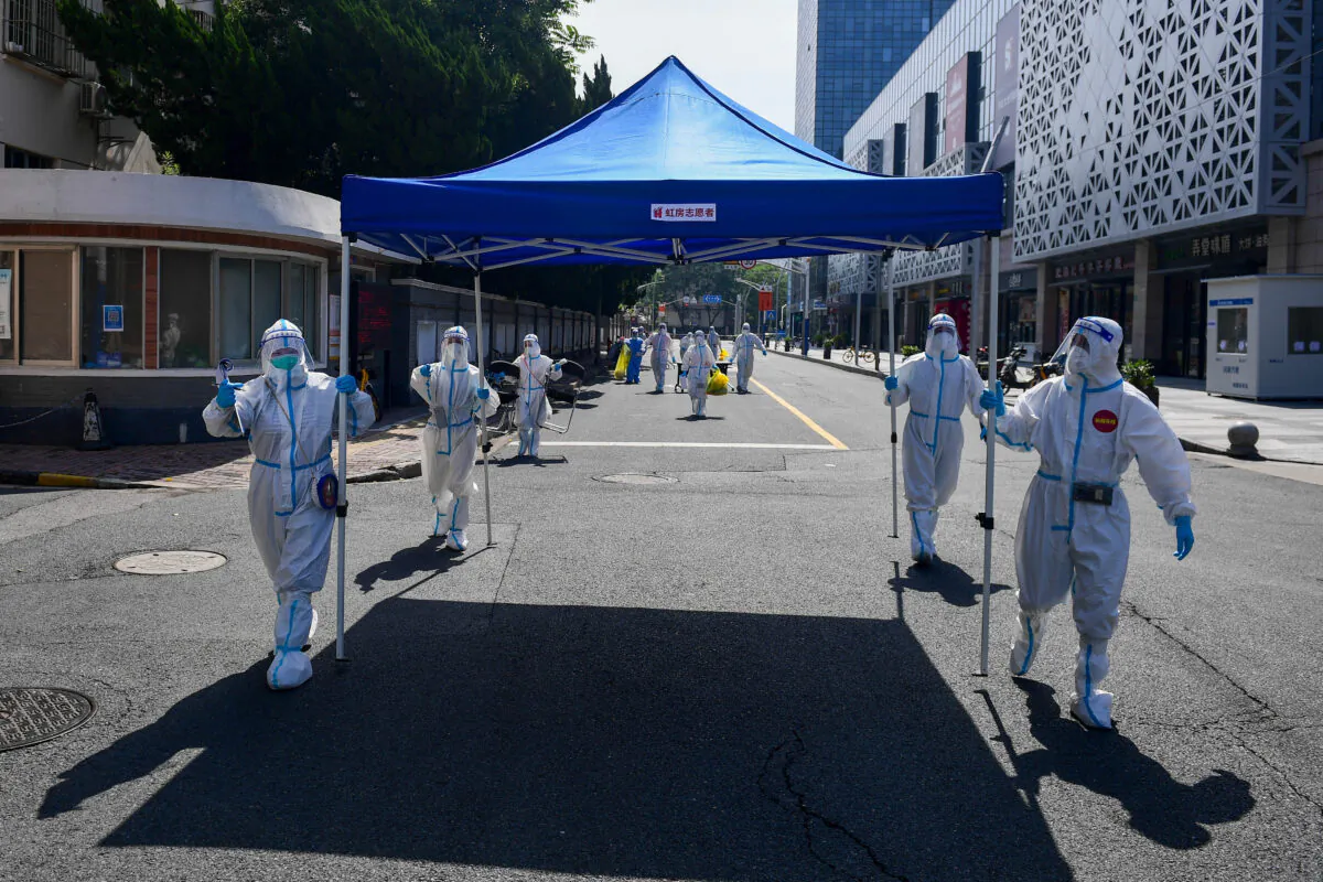 Workers in protective suits move equipment for a makeshift nucleic acid testing site to the next residential area after wrapping up the screening at a compound in Shanghai on May 14, 2022. (cnsphoto via Reuters)