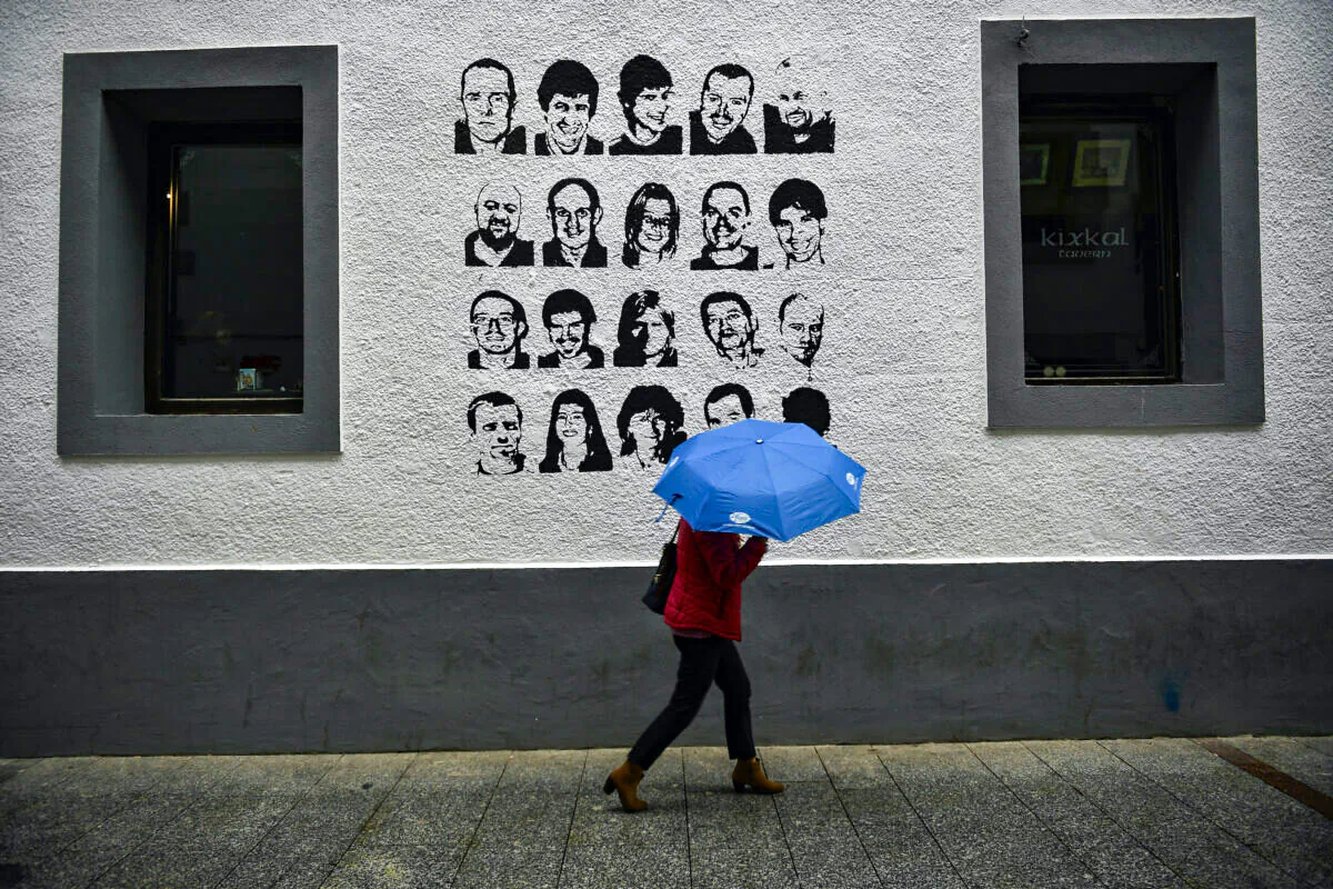 A woman shelters by the rain under an umbrella while walks past close to a wall painted with the portrait of some one basque prisoners of the Basque separatist armed group ETA in the small village of Hernani, northern Spain, on May 2, 2018. (Alvaro Barrientos)