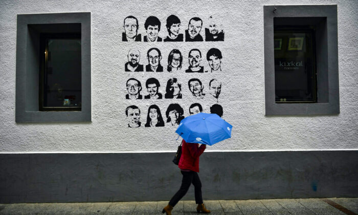 A woman shelters by the rain under an umbrella while walks past close to a wall painted with the portrait of some one basque prisoners of the Basque separatist armed group ETA in the small village of Hernani, northern Spain, on May 2, 2018. (Alvaro Barrientos)