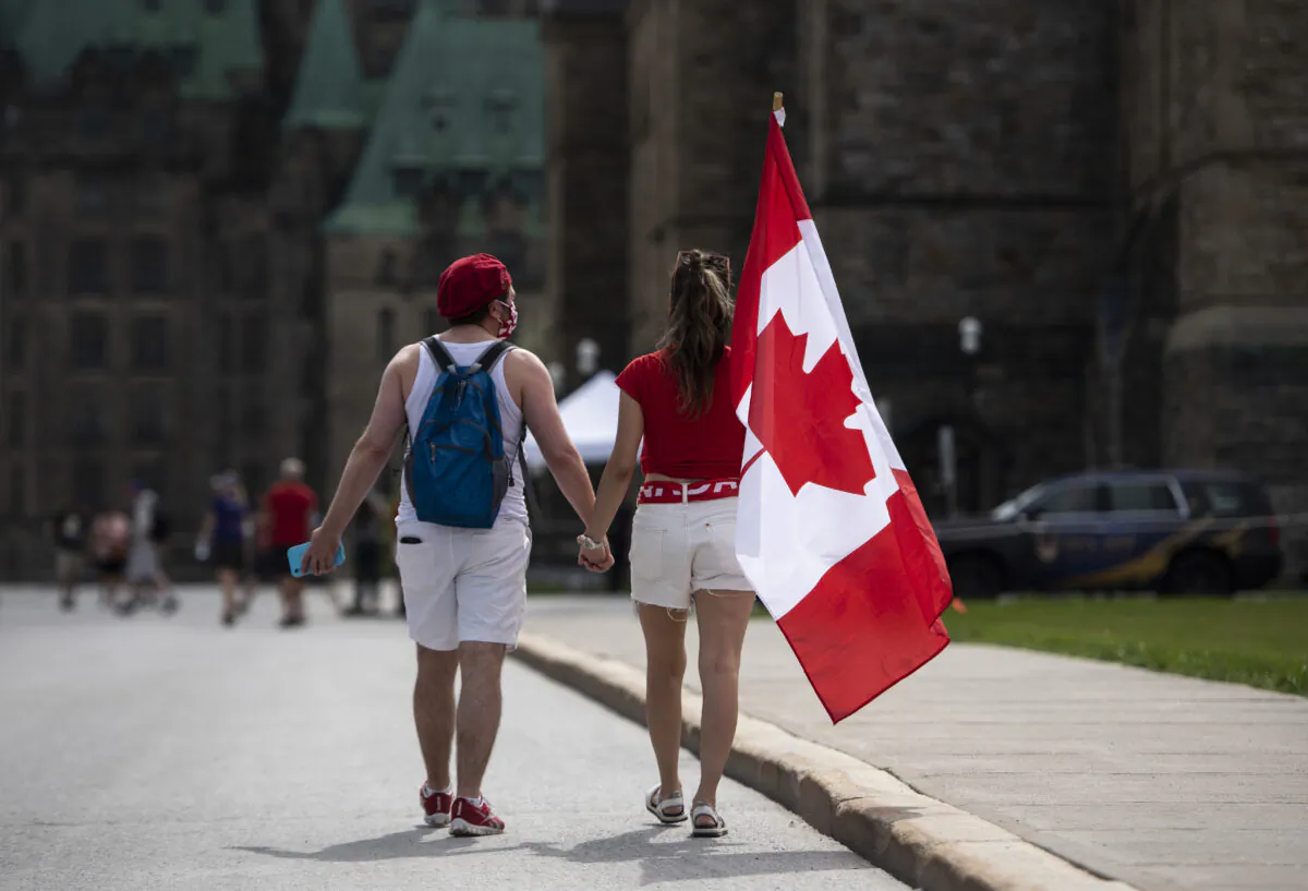 People hold a Canadian flag as they walk on Parliament Hill in Ottawa on Canada Day, July 1, 2021. (The Canadian Press/Justin Tang)