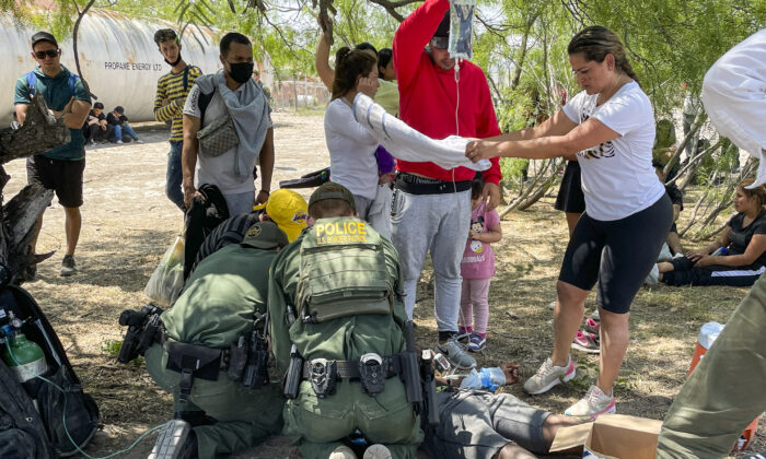 Border Patrol agents provide medical assistance to an illegal immigrant who has heat-related issues, while other agents apprehend a large group of illegal immigrants near Eagle Pass, Texas, on May 20, 2022. (Charlotte Cuthbertson/The Epoch Times)