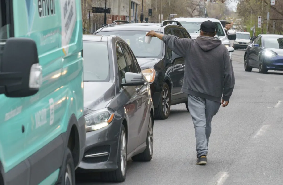 A homeless man panhandles between cars stopped at a red light in Montreal on May 4, 2022. (The Canadian Press/Paul Chiasson)