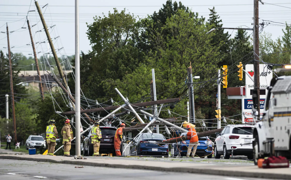 Firefighters and utility workers work among downed power lines, poles, and traffic lights that came down onto the roadway and onto motorists during a major storm, on Merivale Road in Ottawa, on May 21, 2022. (Justin Tang/The Canadian Press)