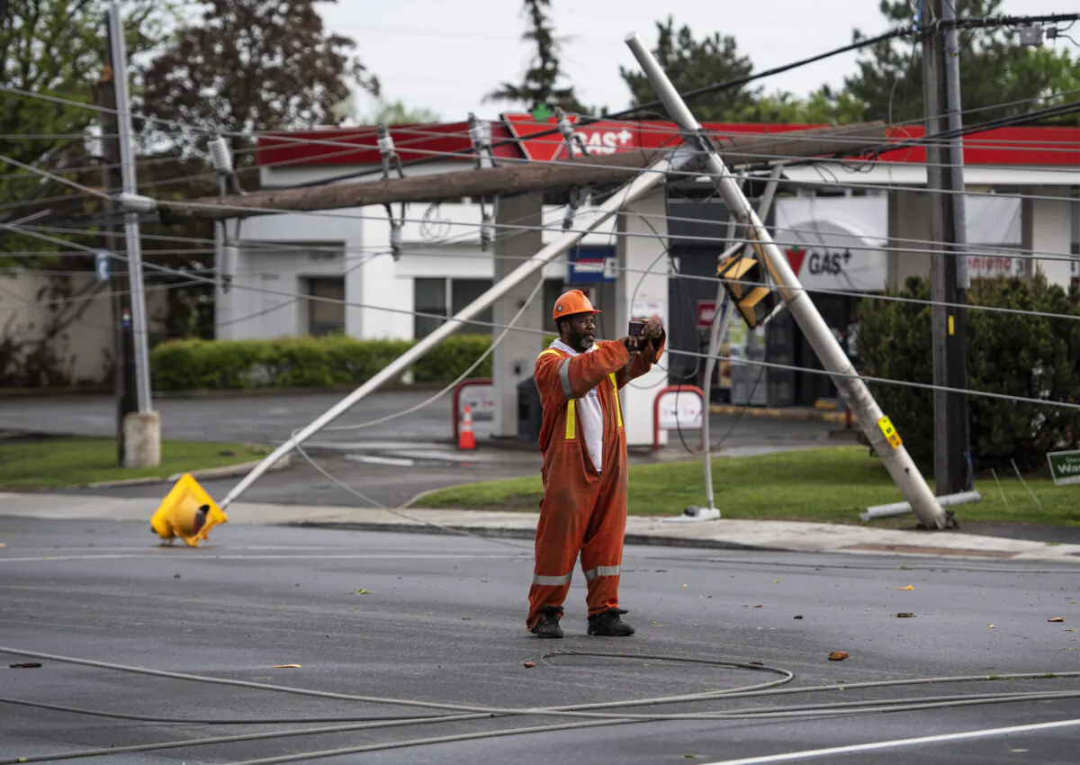 A utility worker documents the damage along the roadway after a major storm took down poles and power lines, on Merivale Road in Ottawa, on May 21, 2022. (The Canadian Press/Justin Tang)