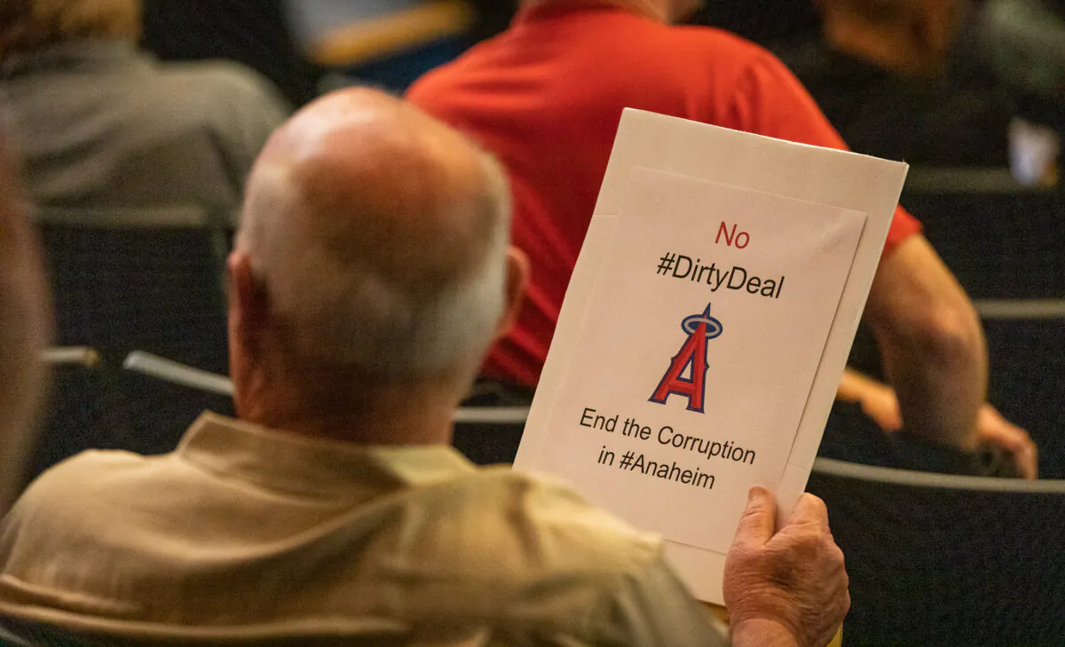 A man attends an Anaheim City Council meeting while holding a sign against Anaheim's pending Angels Stadium deal in Anaheim, Calif., on May 24, 2022. (John Fredricks/The Epoch Times)
