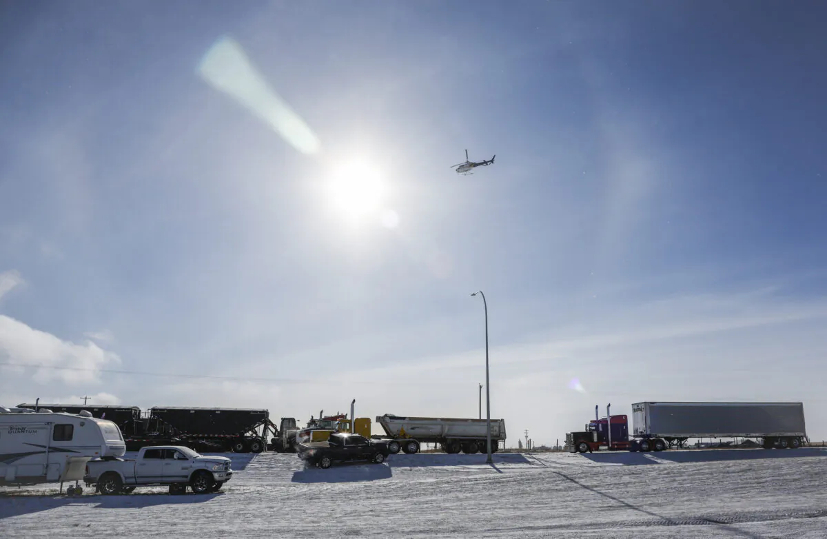 An RCMP helicopter flies over as a truck convoy demonstrating against COVID-19 mandates continues to block the highway at the U.S. border crossing in Coutts, Alberta, on Feb. 2, 2022. (Jeff McIntosh/The Canadian Press)