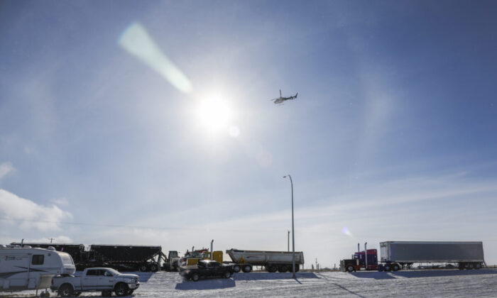 An RCMP helicopter flies over as a truck convoy demonstrating against COVID-19 mandates continues to block the highway at the U.S. border crossing in Coutts, Alberta, on Feb. 2, 2022. (Jeff McIntosh/The Canadian Press)