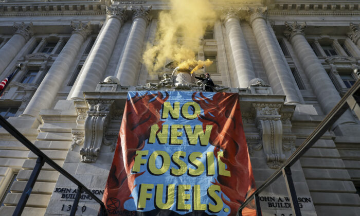 An environmental activist with the group Extinction Rebellion DC scales the Wilson Building next to a sign that reads "No New Fossil Fuels", as part of an Earth Day rally against fossil fuels in Washington on April 22, 2022. (Kevin Dietsch/Getty Images)