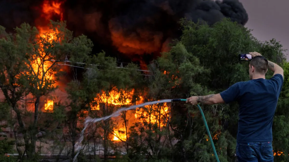 A man sprays down the roof of a neighboring building while also filming the scene of a three-alarm fire at Nox-Crete, Inc., at 1415 S. 20th Street in Omaha, Neb., on May 30, 2022. (Chris Machian/Omaha World-Herald via AP)