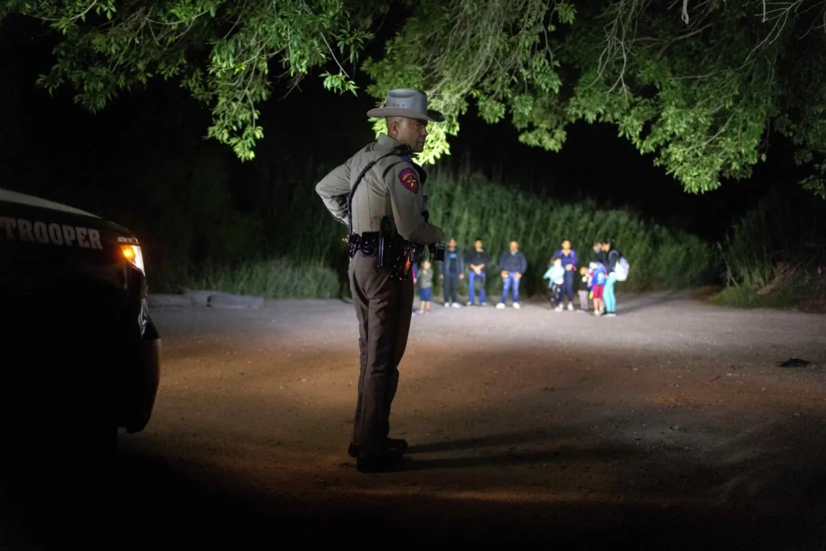 A Texas state trooper watches over illegal aliens as they wait to be taken into custody by U.S. Border Patrol agents in Del Rio, Texas, on May 19, 2021. (John Moore/Getty Images)
