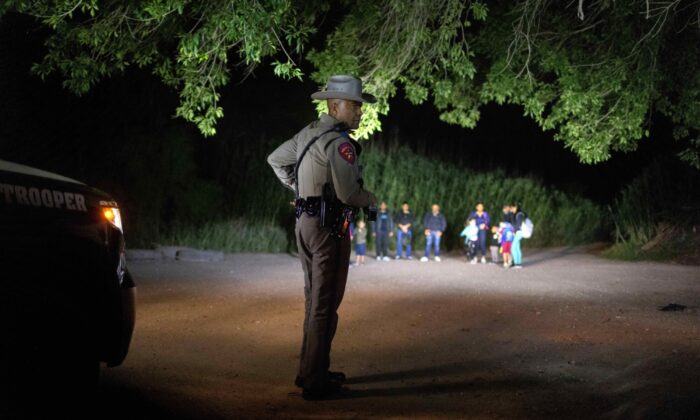 A Texas state trooper watches over illegal aliens as they  wait to be taken into custody by U.S. Border Patrol agents in Del Rio, Texas, on May 19, 2021. (John Moore/Getty Images)