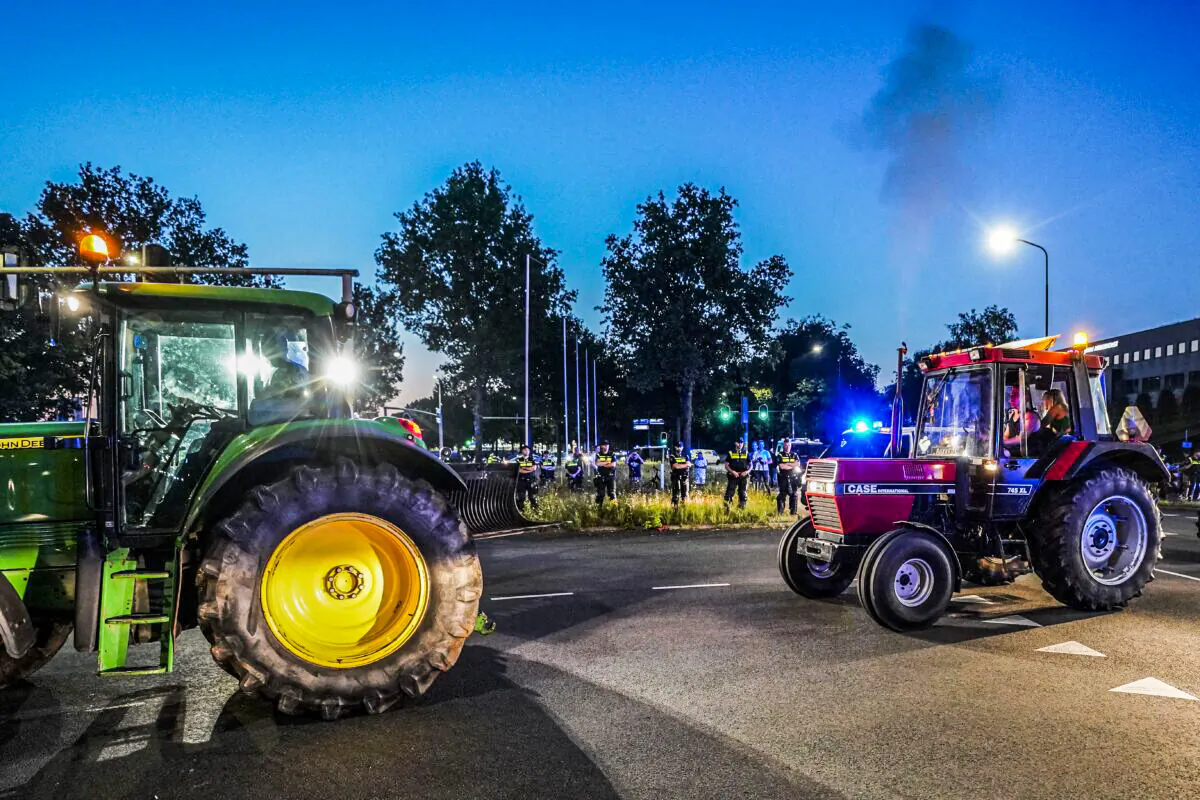 Tractors drive by Dutch police officers standing guard as dutch police close access to Apeldoorn on the A1 highway to stop potential farmers demonstrating against the Dutch government's plans to cut nitrogen greenhouse gas emissions, on 29 June 2022. (Jeroen Jumelet/ANP/AFP via Getty Images)