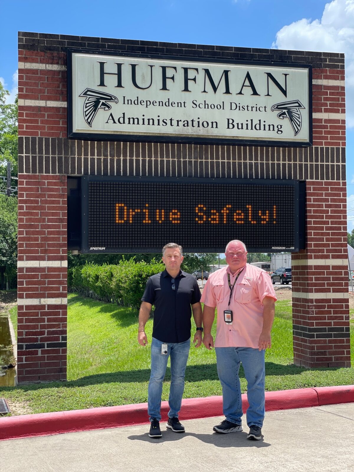 Huffman Independent School District Superintendent of Schools Benny Soileau (left) and Chief of Police David Williams for the Huffman Independent School District (right), stand before the sign for the Huffman County Independent School District Administration Building.