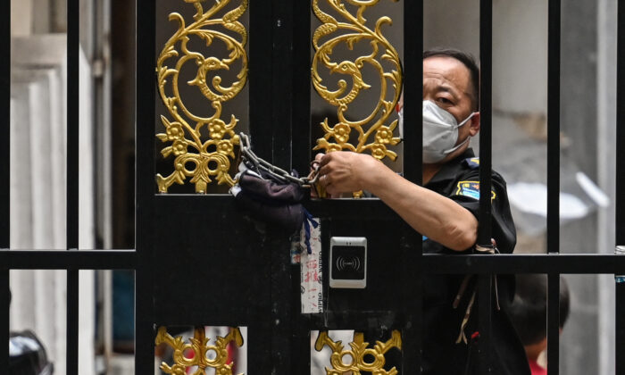 Pracownik ochrony zamyka drzwi łańcuchem w dzielnicy objętej blokadą COVID-19 w dzielnicy Jing'an w Szanghaju 2 czerwca 2022 r. (Hector Retamal/AFP via Getty Images)
