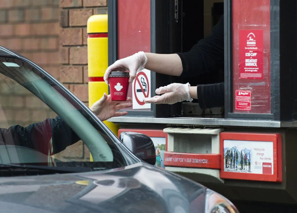 A Tim Hortons employee hands out coffee from a drive-thru window to a customer in Mississauga, Ont., on March 17, 2020. (Nathan Denette/The Canadian Press)