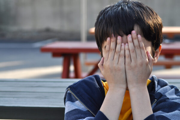 A child stands outside with his hands covering his eyes