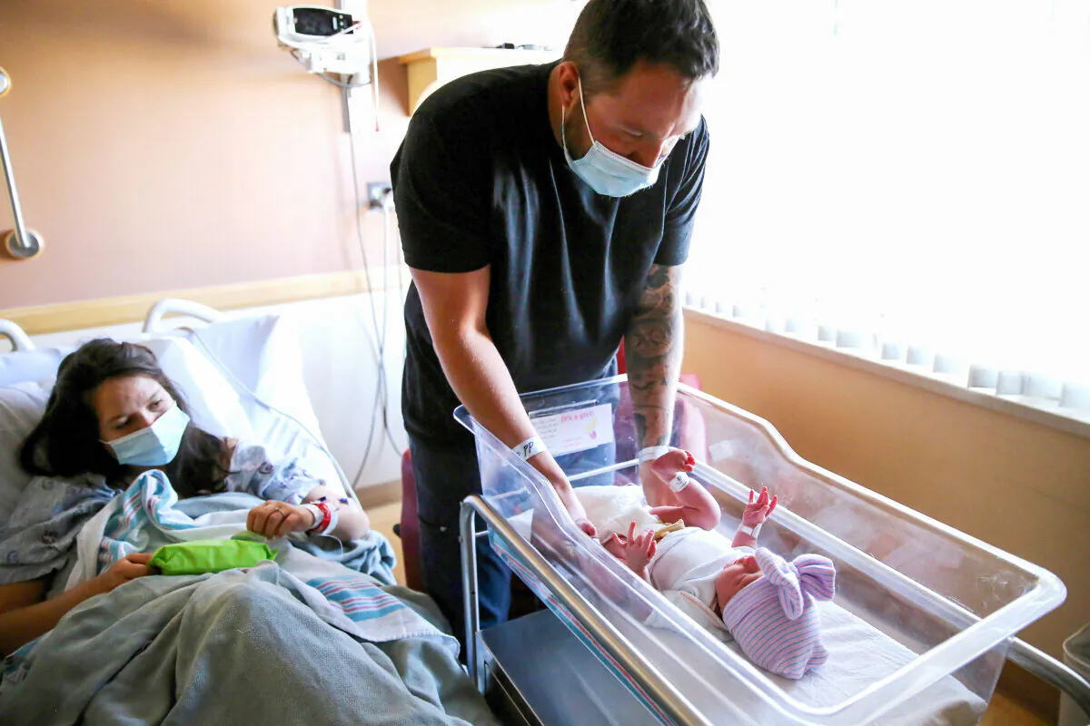 A father prepares to change the diaper of his newborn daughter as his wife looks on in a hospital in Apple Valley, California, on March 30, 2021. (Mario Tama/Getty Images)