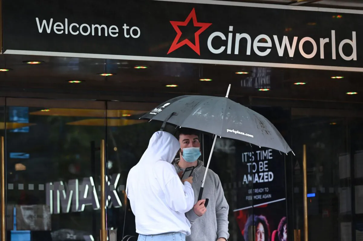 People shelter from the rain under an umbrella outside a Cineworld cinema in Leicester Square in central London on Oct. 4, 2020. (Justin Tallis/AFP via Getty Images)