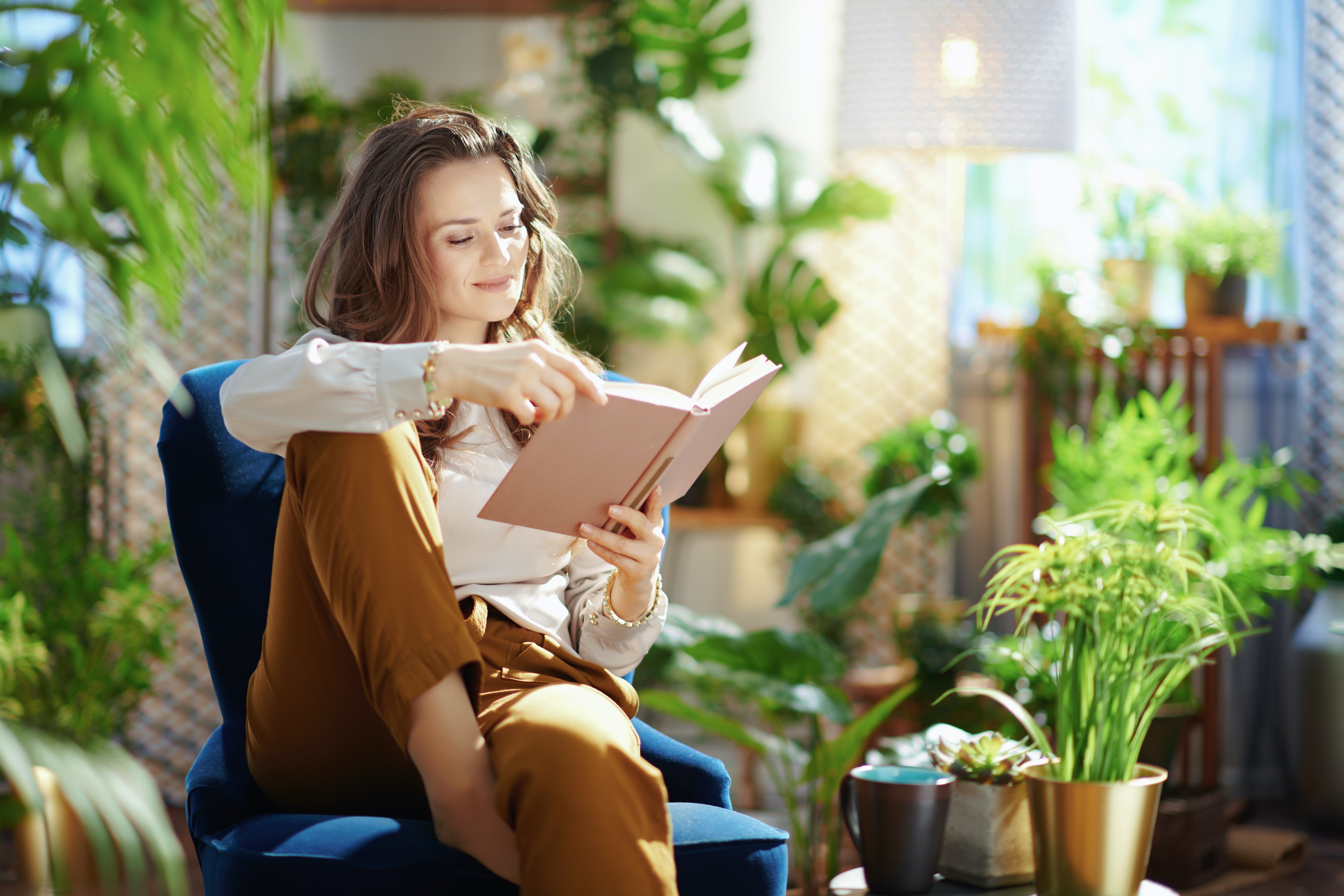 a woman reading in a sunny room full of houseplants