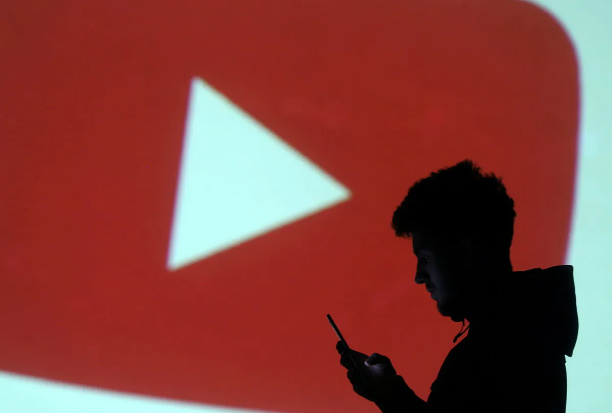 A silhouette of a mobile user next to a screen projection of Youtube logo on March 28, 2018. (Dado Ruvic/Illustration/Reuters)