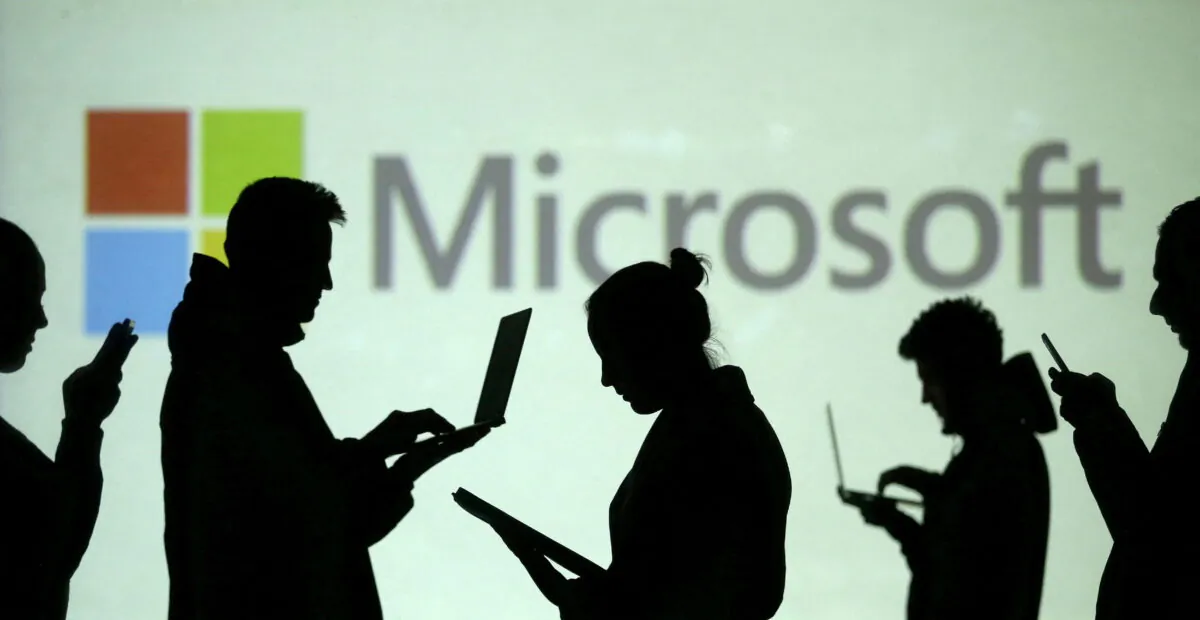 Silhouettes of laptop and mobile device users next to a screen projection of Microsoft logo on March 28, 2018. (Dado Ruvic/Illustration/Reuters)