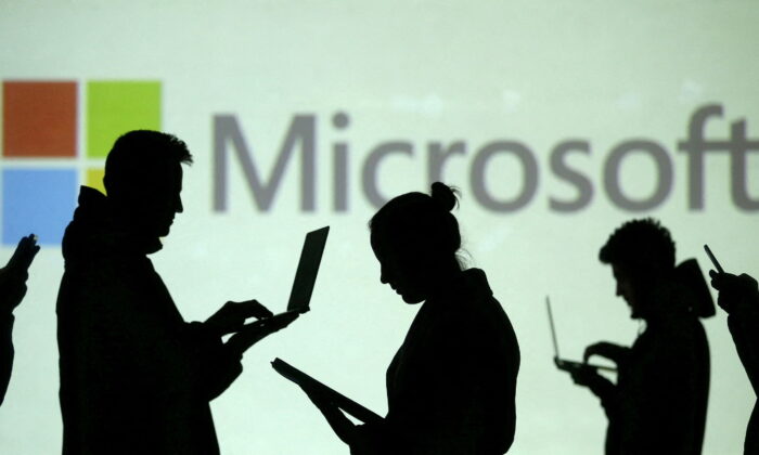 Silhouettes of laptop and mobile device users next to a screen projection of Microsoft logo on March 28, 2018. (Dado Ruvic/Illustration/Reuters)