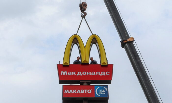 Workers use a crane to dismantle the McDonald's logo and signage from a drive-through restaurant of McDonald's in the town of Kingisepp, Russia, on June 8, 2022. (Anton Vaganov/Reuters)