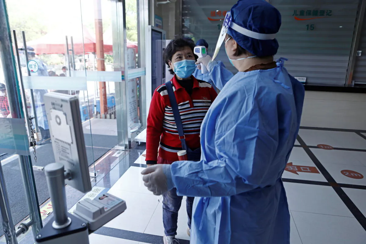 A worker in protective gear measures the body temperature of a woman during a vaccination session for COVID-19 for elderly people at a community health centre in Fengxian district of Shanghai, China on April 21, 2022. (Cnsphoto via Reuters)