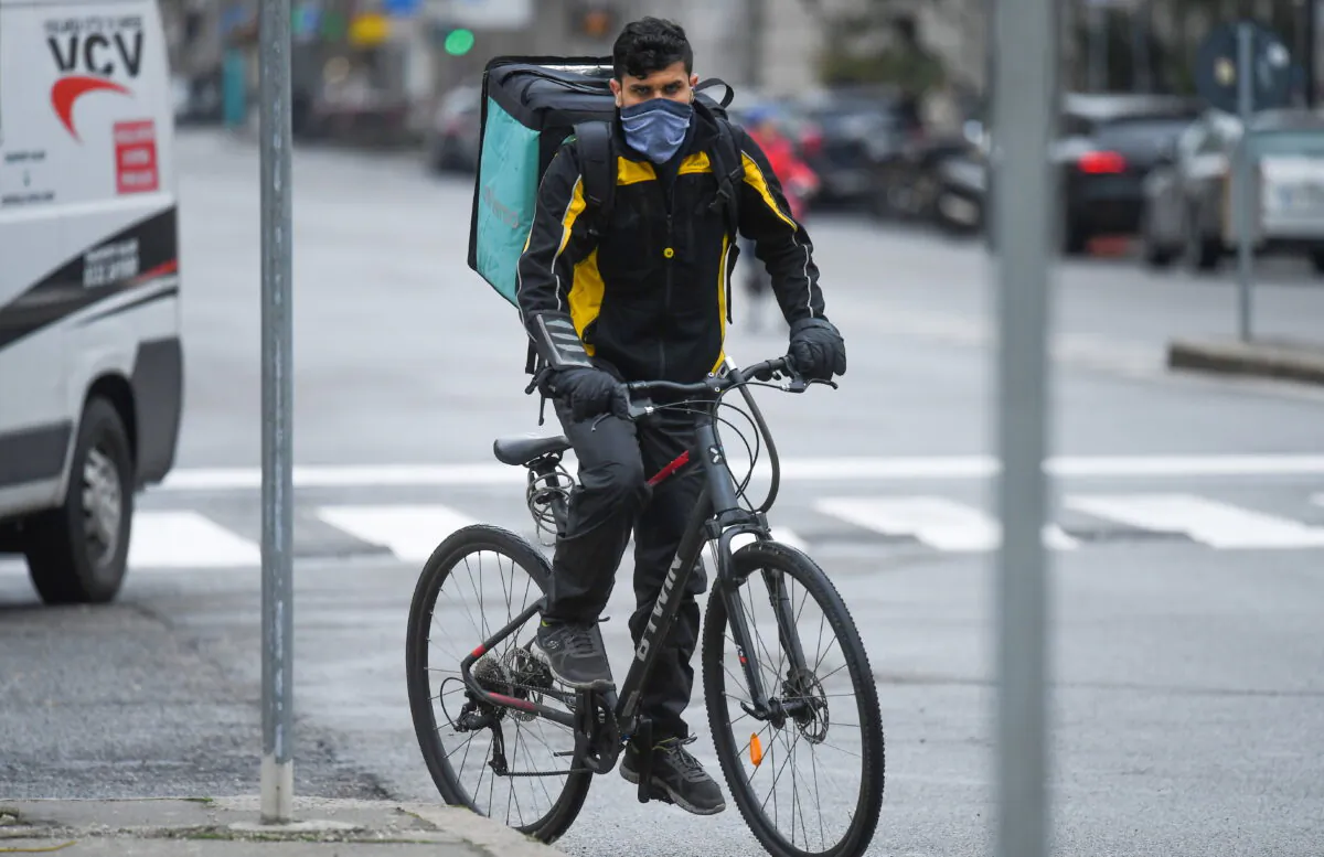 A food delivery employee wearing a protective face mask rides a bike in Milan on March 14, 2020, as the Italian government continues restrictive movement measures to combat the COVID-19 outbreak. (Daniele Mascolo/Reuters)