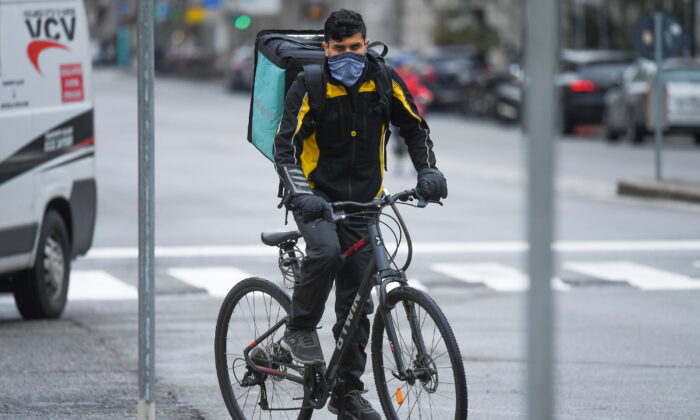 A food delivery employee wearing a protective face mask rides a bike in Milan on March 14, 2020, as the Italian government continues restrictive movement measures to combat the COVID-19 outbreak. (Daniele Mascolo/Reuters)