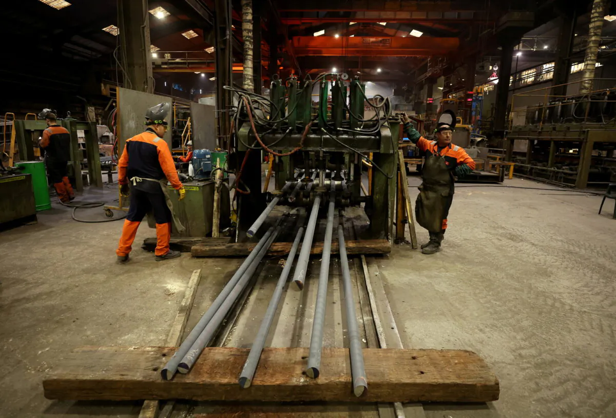Workers stand next to a machine cutting newly manufactured bars of steel at the United Cast Bar Group's foundry in Chesterfield, Britain, on April 12, 2022. (Phil Noble/Reuters)