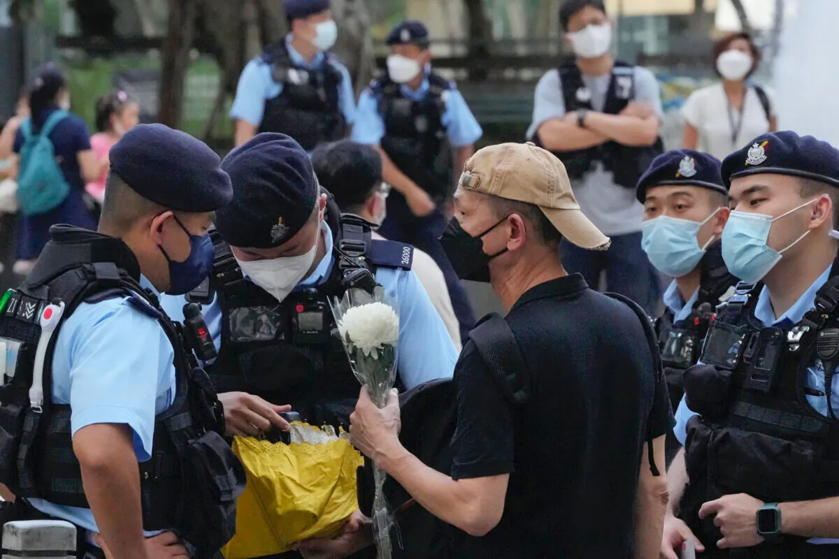 Police officers stop and search a man holding a flower at the Hong Kong's Victoria Park, Saturday, June 4, 2022. Dozens of police officers patrolled Hong Kong's Victoria Park on Saturday after authorities for a second consecutive third banned public commemoration of the anniversary of the Tiananmen Square crackdown in 1989, amid a crackdown on dissent in the city. (AP Photo/Kin Cheung)