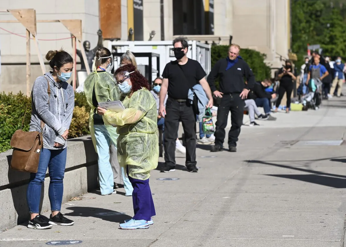 A health-care worker takes information as people line up at a COVID assessment centre during the COVID-19 pandemic, in Toronto on Sept. 18, 2020. (The Canadian Press/Nathan Denette)