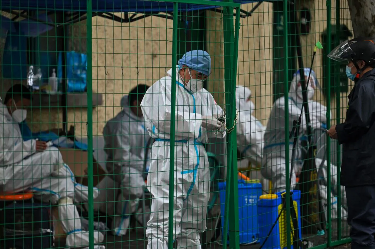 A worker wearing personal protective equipment (PPE) padlocks a fence securing a residential area under COVID-19 lockdown in the Huangpu district of Shanghai on June 13, 2022. (Hector Retamal/ AFP via Getty Images)