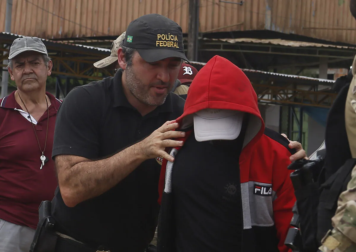 A federal police officer escorts a suspect towards a river in the area where Indigenous expert Bruno Pereira and freelance British journalist Dom Phillips disappeared, in Atalaia do Norte, Amazonas state, Brazil, on June 15, 2022. (Edmar Barros/AP Photo)