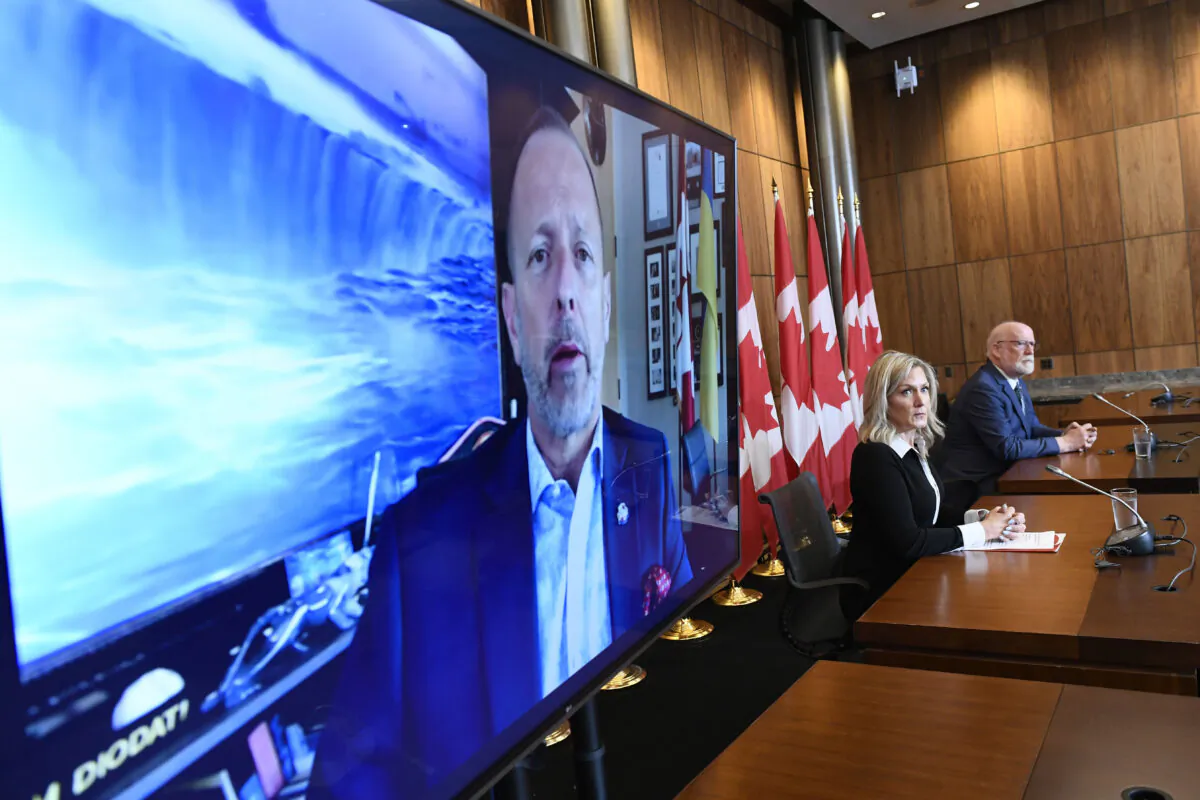 An image of Niagara Falls is seen behind Niagara Falls, Ont. Mayor Jim Diodati as he appears via video conference alongside Barbara Barrett, Executive Director of the Frontier Duty Free Association, and NDP MP for South Okanagan—West Kootenay Richard Cannings (R) during a news conference as leaders and businesses in border communities speak out against the federal government’s vaccination requirements at land borders, in Ottawa, on June 15, 2022. (The Canadian Press/Justin Tang)