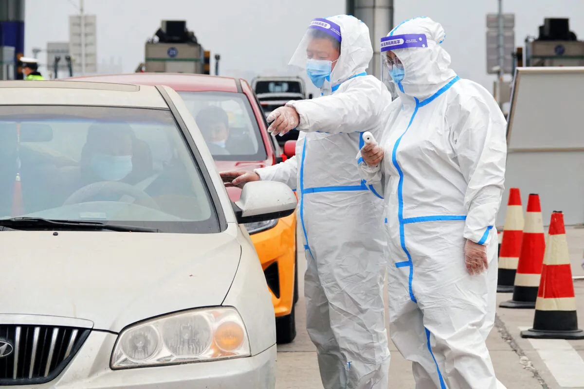 A staff member wearing personal protective equipment (PPE) directs drivers as they check people's nucleic acid test results and health codes at a highway toll station in Yantai, Shandong Province, China, on March 16, 2022.(STR/AFP via Getty Images)