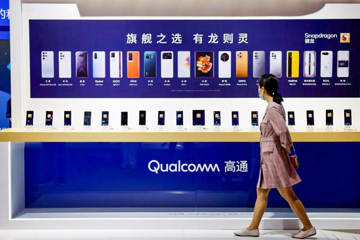 A woman walks past a counter displaying mobile phones at the Qualcomm booth during the 2021 China International Fair for Trade in Services (CIFTIS) in Beijing on Sept. 4, 2021. (Florence Lo/Reuters)