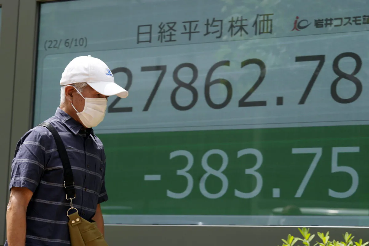 A man wearing a protective mask walks in front of an electronic stock board showing Japan's Nikkei 225 index at a securities firm on June 10, 2022, in Tokyo. (AP Photo/Eugene Hoshiko)