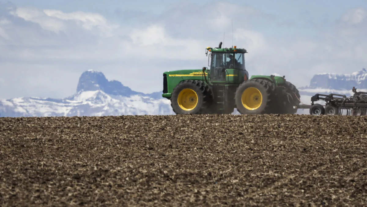 A farmer drives a wheat planting rig, with the Rocky Mountains as a backdrop, near Cremona, Alta., on May 6, 2022. (The Canadian Press/Jeff McIntosh)